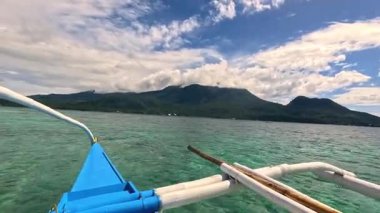 Point of view riding Bangka boat across tropical seas, Camiguin island volcanic mountain range and green landscape, Asia Philippines backpacking, holiday tourism vacation