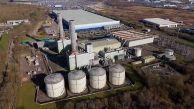 Aerial drone view of power plant, station with chimney stacks, gas burning chamber, fuel storage silos and industrial buildings, Corby England UK