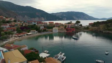 Asos balıkçı kasabasının hava aracı görüntüsü, gün batımında turistik bir yer. Yatlar ve deniz kenarındaki küçük evler, dağlık bölge, Kefalonia, Yunanistan ve Avrupa 'daki berrak mavi sular tatil beldesi turizmi