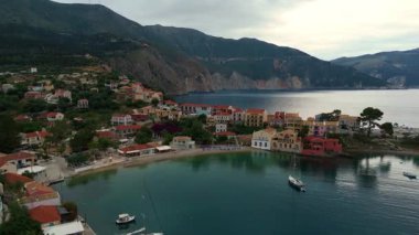 Asos balıkçı kasabasının hava aracı görüntüsü, gün batımında turistik bir yer. Yatlar ve deniz kenarındaki küçük evler, dağlık bölge, Kefalonia, Yunanistan ve Avrupa 'daki berrak mavi sular tatil beldesi turizmi