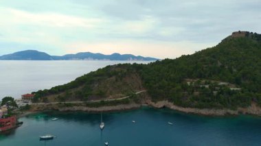 Asos balıkçı kasabasının hava aracı görüntüsü, gün batımında turistik bir yer. Yatlar ve deniz kenarındaki küçük evler, dağlık bölge, Kefalonia, Yunanistan ve Avrupa 'daki berrak mavi sular tatil beldesi turizmi