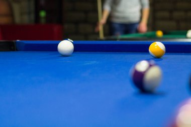 Bilardo oyunu devam ediyor, toplar mavi masa örtüsünde.