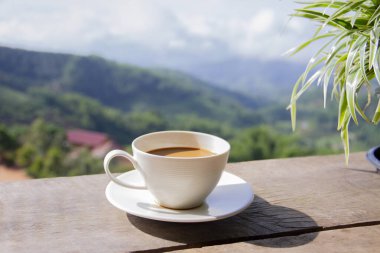 Dağın arkasındaki eski ahşap masada beyaz kahve, sabah vakti içmek, yiyecek ve içecek konsepti.