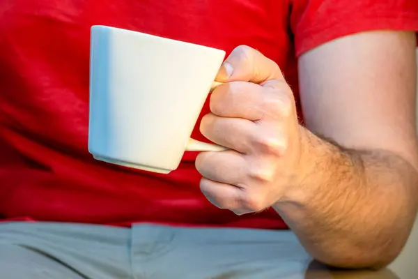 Caucasian latin man, sitting, dressed in a red t-shirt and jeans. Holding a white cup.