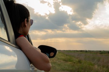 Genç Latin gezgin, arabanın camında gün batımını seyrediyor..