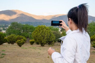 Güzel ve doğal Latin kadın cep telefonuyla manzaranın fotoğraflarını çekiyor..