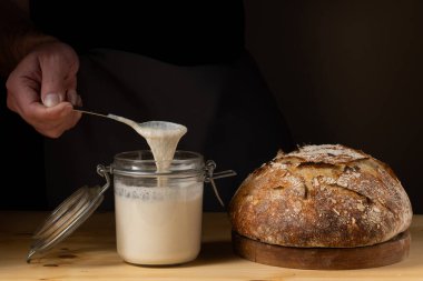 Cam kavanozdaki ekşi hamuru gösteren genç bir adamın elleri. Yanında ekşi ekşi ekmek vardı..