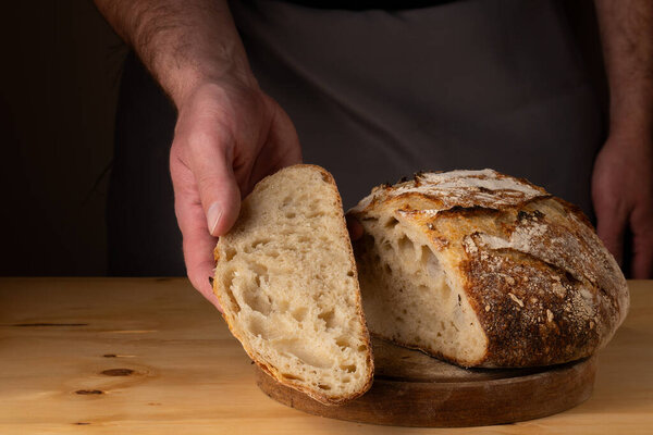 The hands of a young man handling sourdough bread, highlighting the bread with beautiful golden tones against the dark background.