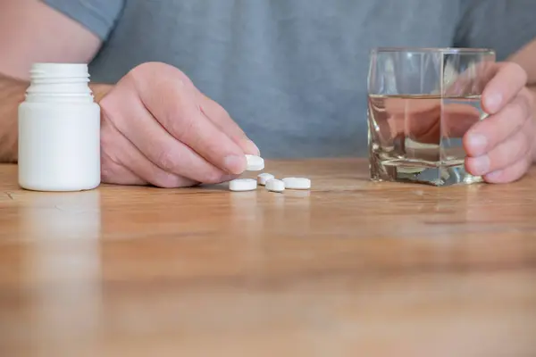 Person taking their medicine sitting at the kitchen table.