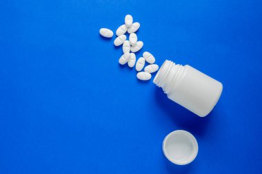 Mavi arka planda beyaz haplar, şişelerinin yanında..