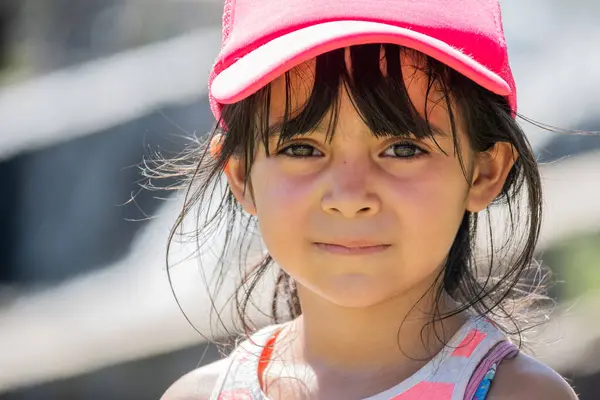 Seyahatte olan Latin bir çocuğun çok yakın bir portresi. Kız pembe bir şapka takıyor. Çok ciddi bir yüzle kameraya bakıyor..
