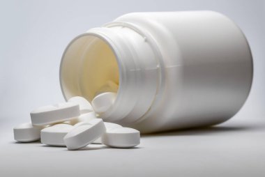 Çok hafif bir arka planda hapları olan açık bir ilaç şişesi..