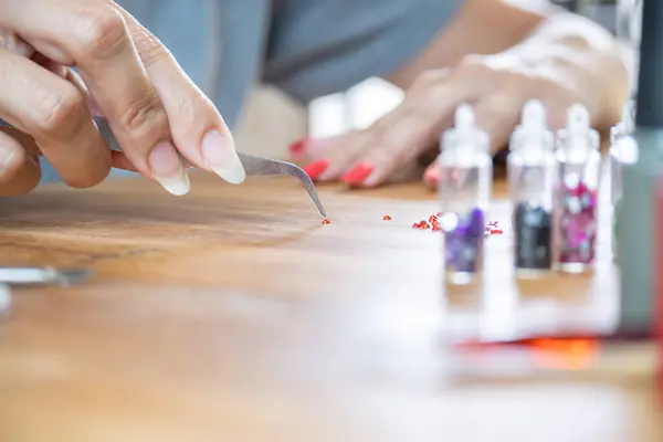 Genç bir kadın, masaya çivi çakmak için cımbızla küçük bir elmas seçiyor..