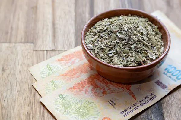 Concept of the cost of yerba mate. Argentine pesos with yerba mate in a bowl.