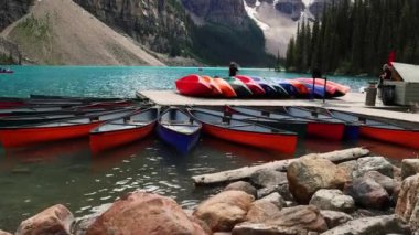 Moraine Gölü 'nün parlak mavi buzul sularına bakıyoruz. Uzun, sivri dağlar ve yoğun çam ormanları, Banff Ulusal Parkı, Alberta, Kanada. Gölde kanolar var. Yüksek kalite 4k görüntü
