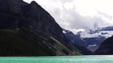 Louise Gölü 'nün açık mavi buzul suları bulutlu bir günde, Banff Ulusal Parkı, Alberta, Kanada. Etrafı yüksek dağlar, buzullar ve yoğun çam ormanlarıyla çevrili. Yüksek kalite 4k görüntü