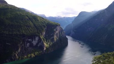 Gün batımında Norveç 'te Geirangerfjord manzarası. Norveç fiyortlarının üzerinde yükselen uzun dağlar ve bulutların arasında parlayan güneş ışınları. Yüksek kalite 4k görüntü