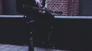 Siyah elbiseli, gitarlı ve gözlüklü vahşi bir adam.