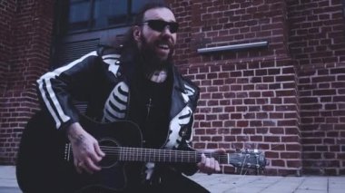 Siyah elbiseli, gitarlı ve gözlüklü vahşi bir adam.