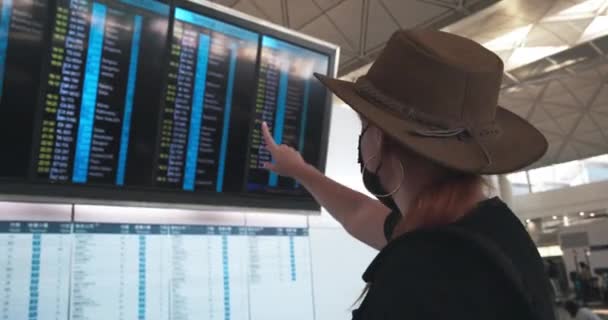 穿着面具和帽子的女孩看着机场的离境板 — 图库视频影像