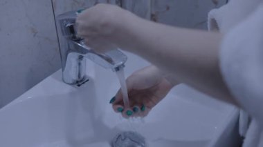 Kadın ellerini lavaboya yakın çekimde yıkıyor.