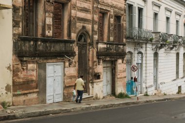 Asuncion, Paraguay 'da şehrin zengin tarihini ve benzersiz mimari tarzını gözler önüne seren yıpranmış binalarla çevrili bir sokakta gezinen bir insan..