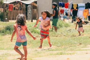Asuncion, Paraguay - 21 Ağustos 2023: Bir grup çocuk, Paraguay 'ın çimenli bir bölgesinde neşeli bir şekilde koşuyor, çizgilerde asılı parlak giysiler ve güneşli bir öğleden sonra sıcaklığıyla.