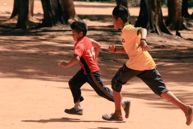 Asuncion, Paraguay - 21 Ağustos 2023: İki enerjik çocuk güneşli, kumlu bir alanda birbirleriyle yarışıyor, ağaçlarla çevrili, Paraguay 'da neşeli bir öğleden sonranın keyfini çıkarıyorlar.