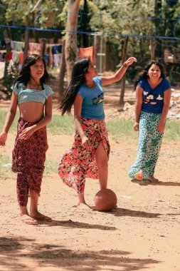 Asuncion, Paraguay - 21 Ağustos 2023: Üç kız Paraguay 'ın kırsal kesiminde canlı bir futbol maçının keyfini çıkarıyor, parlak güneşin altında geleneksel etek giyerken neşeli ruhlarını sergiliyorlar..