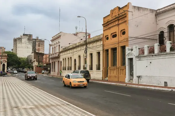 Asuncion 'da bir caddede farklı renklere boyanmış çeşitli tarihi binalar, yol boyunca seyahat eden arabalar, hepsi bulutlu bir gökyüzünün altında.