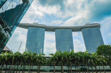 Singapur 'un ufuk çizgisi bulutlu bir akşamda yemyeşil palmiye ağaçları arasında Marina Körfezi Kumları' nı gösteriyor..