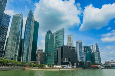 Parlak gökdelenler su kenarındaki güneş ışığını yansıtıyor, Singapur 'un etkileyici kentsel manzarasını ve mimari yeniliklerini gözler önüne seriyor..