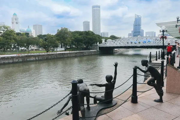 Canlı nehir kıyısında, yemyeşil ve Singapur 'un ufuk çizgisi ile çevrili, su kenarında oynayan çocukların heykelleri yer alıyor..