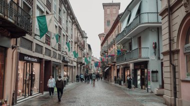 Alba, İtalya - 27 Ekim 2024: Ziyaretçiler, İtalya 'nın Alba kentinin renkli bayraklarının dükkanların ve kafelerin üzerinde asılı olduğu ve yağmurlu havaya rağmen canlı bir atmosfer yarattığı resimli caddelerini keşfediyorlar..