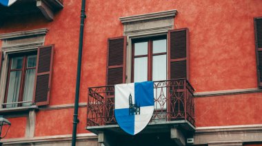 Alba, İtalya - 27 Ekim 2024: Alba 'da canlı bir bina mavi ve beyaz armalı çarpıcı bir balkon sergiliyor. Mimari ayrıntılar İtalyan güneşinin cazibesini vurguluyor..