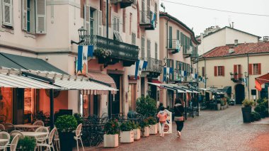 Alba, İtalya - 27 Ekim 2024: Ziyaretçiler, kafelerin ve balkonların büyüleyici binaları süslediği ve akşam ışıklarının ılık bir ortam yarattığı İtalya 'nın Alba kentinin pitoresk sokaklarında sakin bir yürüyüş yapıyorlar..