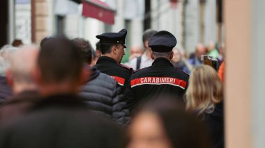 Alba, İtalya - 27 Ekim 2024: İnsanlar hareketli bir öğleden sonra geçerken İtalya 'nın Alba kentinde hareketli bir caddede yürüyen üniformalı iki polis memuru. Titreşimli atmosfer toplumsal bağlılık ve güvenliği vurguluyor.