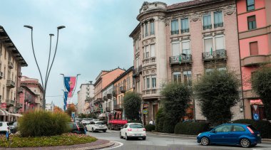 Alba, İtalya - 27 Ekim 2024: Alba İtalya 'da canlı bir cadde modern araçların arasına yerleştirilmiş zarif tarihi binaları gösteriyor. Bulutlu gökyüzü canlı şehir yaşamına yumuşak bir ışık tutuyor, büyüleyici alanları yansıtıyor..