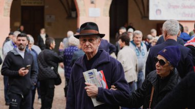 Alba, İtalya - 27 Ekim 2024: Şapkalı yaşlı bir adam Alba, İtalya 'da bir kalabalığın arasında gazete tutuyor. Canlı pazar günü yerel halkın atmosferden zevk aldığını ve birbirleriyle etkileşimde olduğunu gösteriyor..