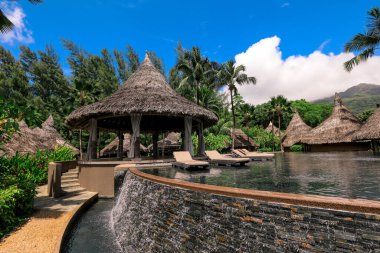 Seyşeller 'de sazdan kulübeler, sakin bir havuz ve parlak bir gökyüzü altında canlı bir yeşillik içeren tropik bir kaçamak..