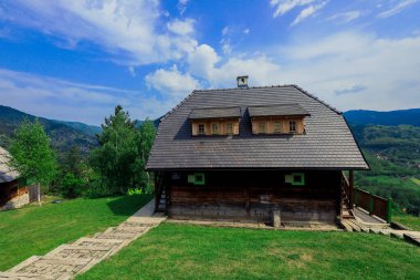 Drvengrad Köyü 'nde berrak mavi gökyüzünün altında yemyeşil tepelerle çevrili taşralı ahşap bir ev gururla duruyor..