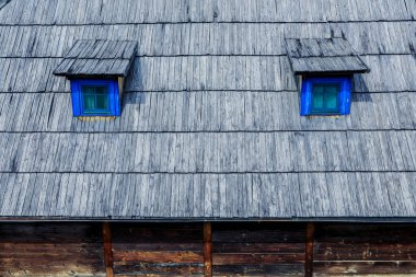 Ahşap çatıda, Drvengrad Köyü 'nün kırsal mimarisini gün ışığında yansıtan iki mavi pencere bulunuyor..