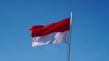 Kumaştan yapılmış kırmızı ve beyaz bir bayrak mavi gökyüzünde dalgalanıyor..