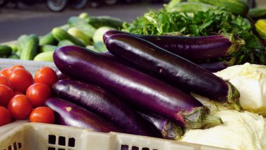 Geleneksel bir pazarda çeşitli yığınlarda mor patlıcan ve taze sebzeler.