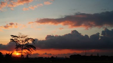 Yağmur mevsiminde yoğun bulutlarla kırmızımsı gün batımı.