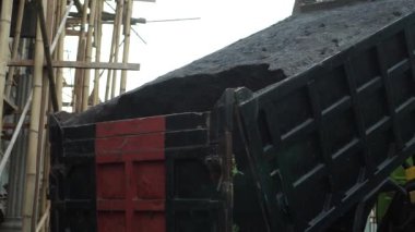 İnşaat alanında bir kamyonun arkasından siyah kum boşaltılıyor..