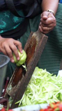Yaşlı bir kadının geleneksel aletlerle sebzeleri elle doğrarken çekilmiş yavaş çekim videosu.
