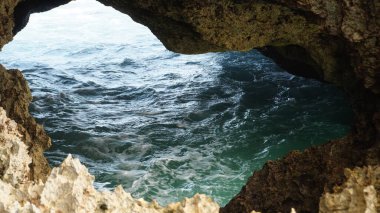 Dalgalanan ve mağara odasında küçük dalgalar oluşturan engebeli bir duvar dokusu ve mavi bir su yüzeyi olan bir mağara..
