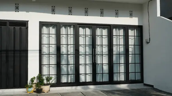 Açık, gölgelenmemiş bir verandası ve garaj kapısına bitişik birkaç saksı bitkisi olan bir binanın ön cam kapıları ve pencereleri.