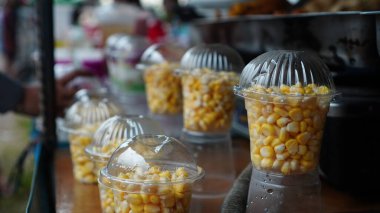Atıştırmalık mısır temiz plastik bardaklarda güzelce sunulur. Sarı çekirdekler kubbe kapaklarıyla mühürlenmiş. Bu da bir satıcıda müşteriler için kap-kaç yiyecek olduğunu gösteriyor..